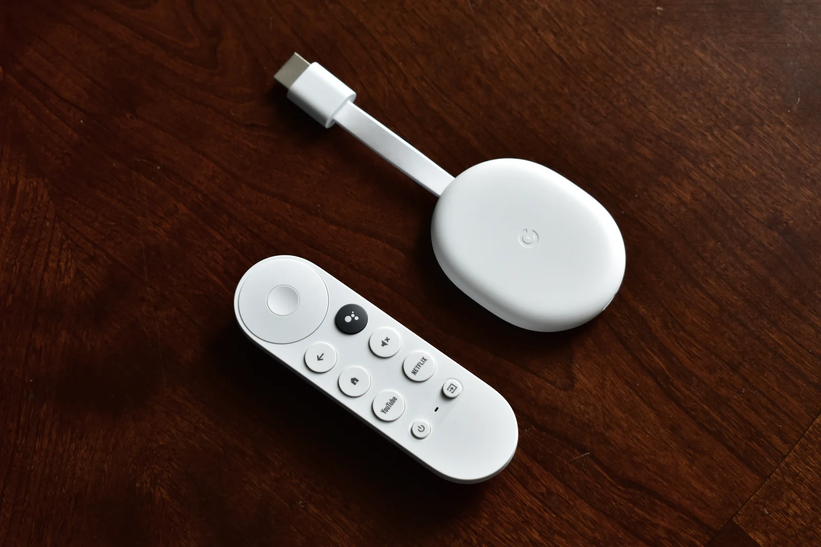 Chromecast avec Google TV et télécommande posés sur une table en bois dans un salon