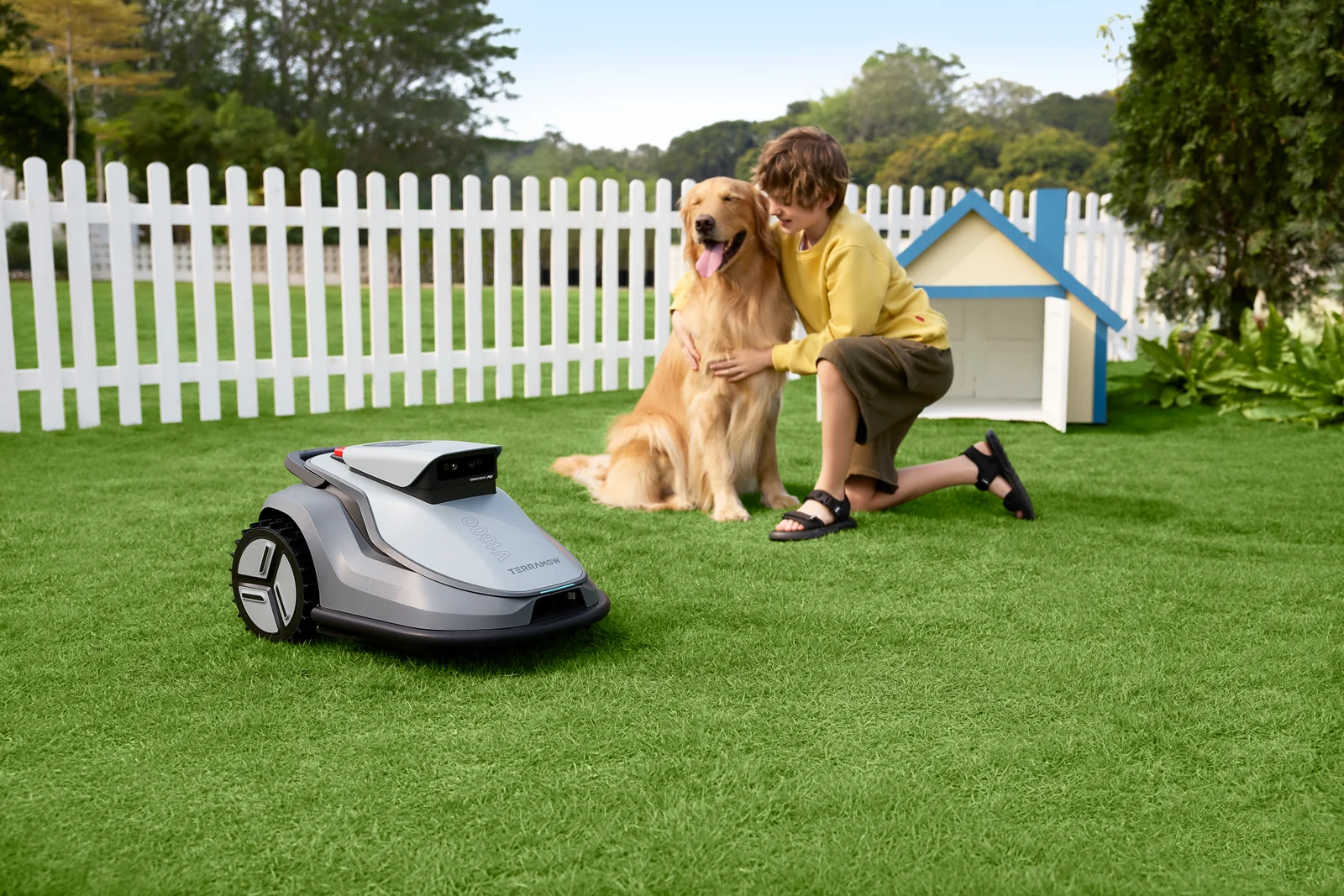 Un enfant et un chien à proximité d'un robot tondeuse TerraMow dans un jardin clôturé