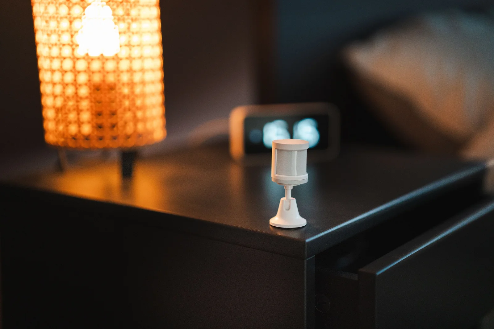 Détecteur de mouvement connecté posé sur une table de chevet en bois dans une chambre lumineuse
